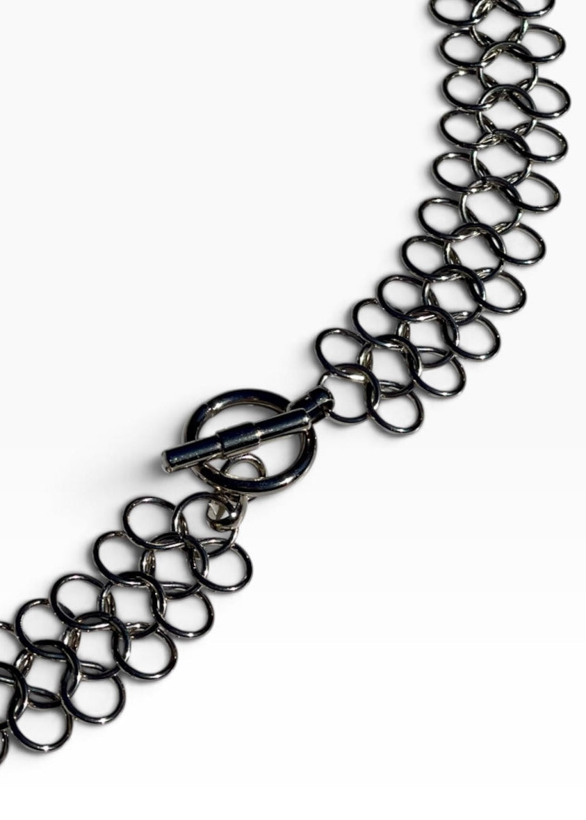 A close-up of a dark metallic chain bracelet with a unique interlocking ring design and a toggle clasp, shown on a clean white background.