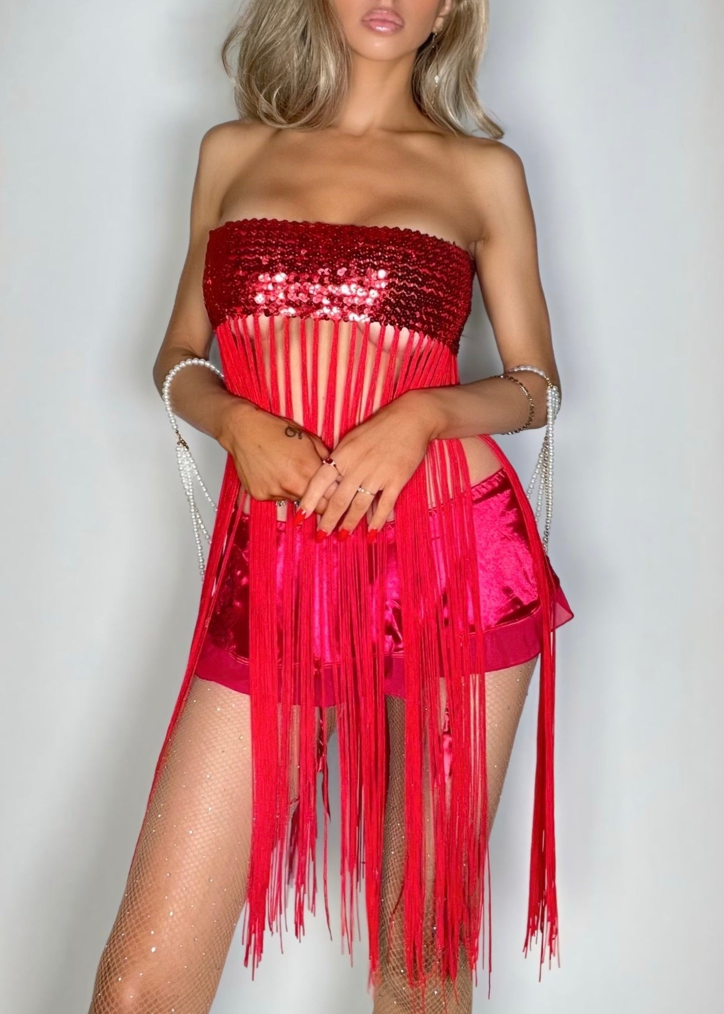 Woman wearing a red strapless dress with fringe details against a plain background