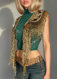 Person wearing a green top with a gold fringe accessory against a neutral background