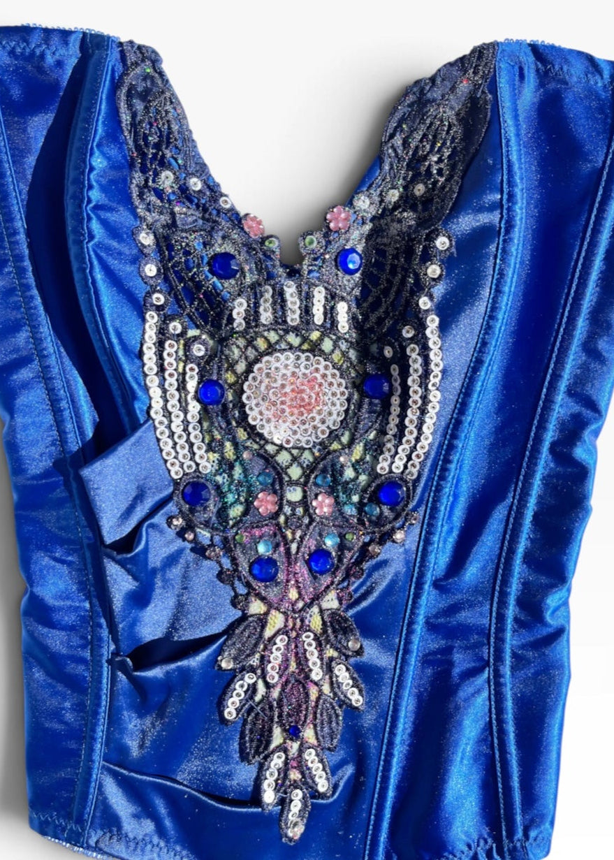 A royal blue satin corset bustier with an elaborate, ornate beaded and embellished yoke featuring silver, pink, and blue rhinestones, shown against a plain white background.