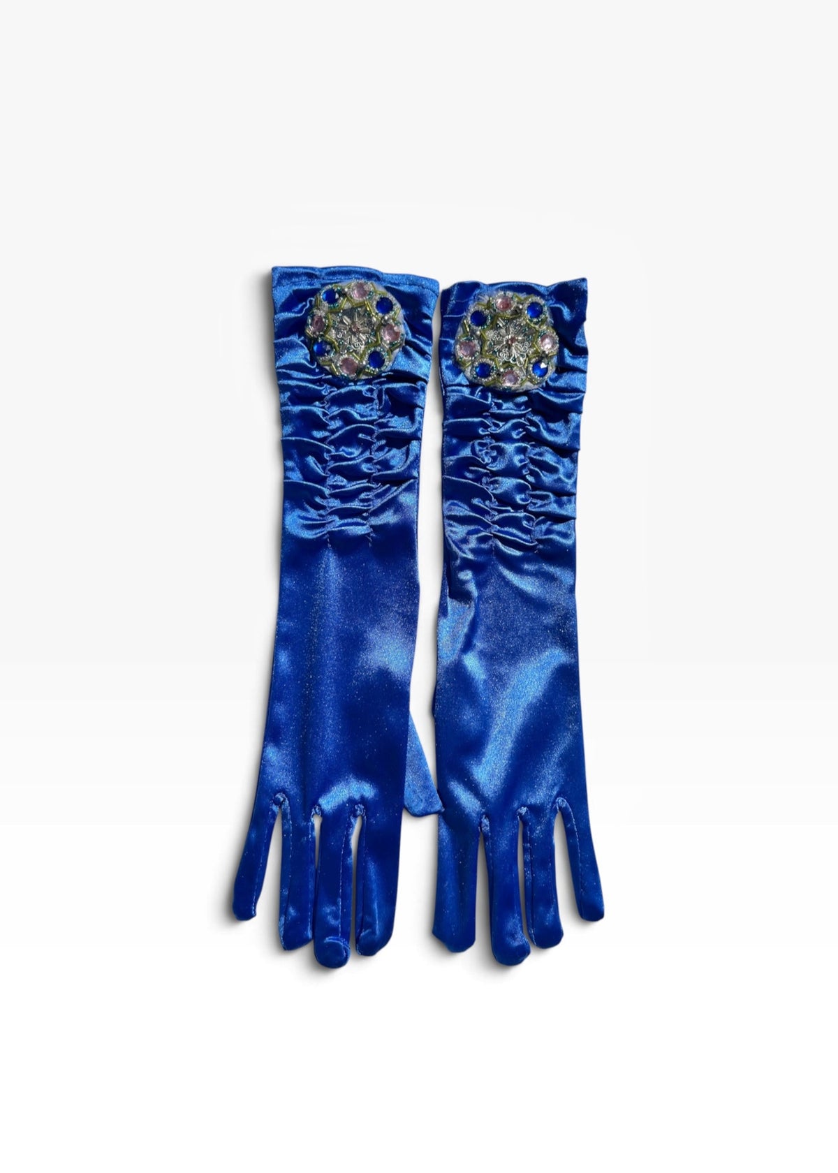 A pair of royal blue satin opera gloves with ruched detailing and jeweled circular embellishments near the cuffs, displayed flat against a white background.