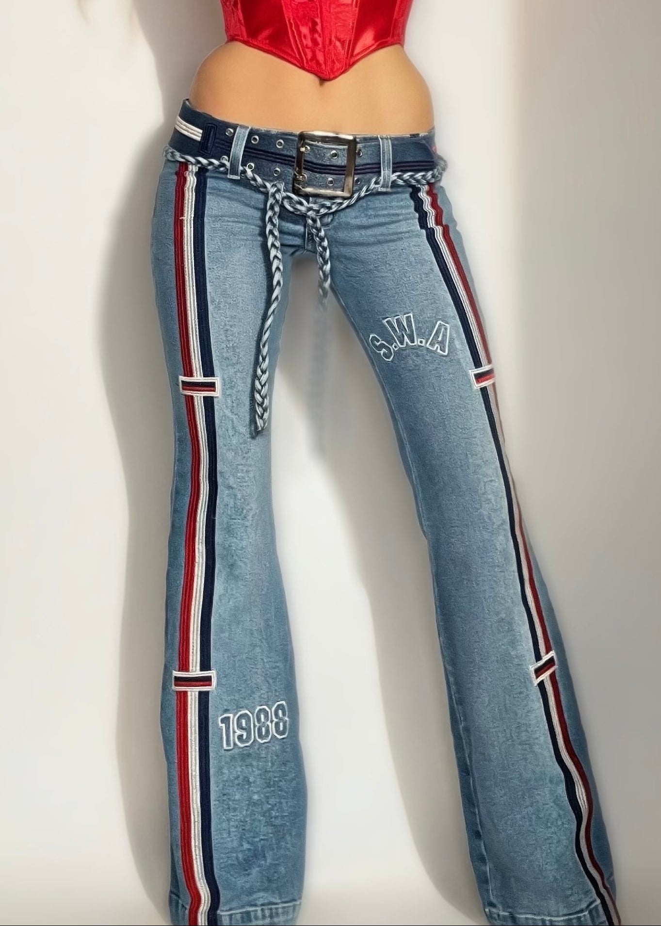 Person wearing a red top and blue jeans with a striped waistband on a plain background