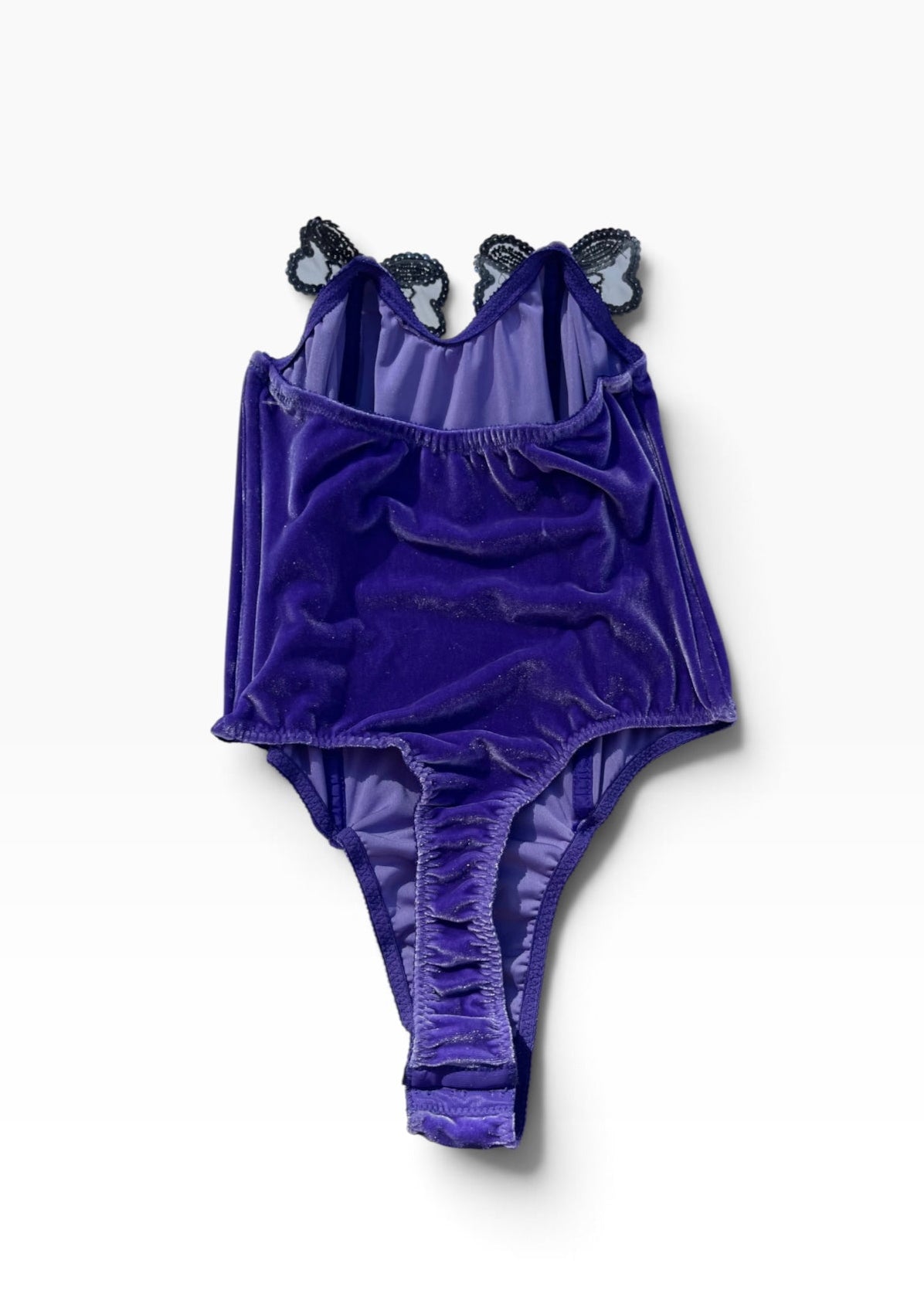 A purple velvet one-piece swimsuit with ruffled straps and butterfly embellishments on the shoulders, laid flat against a white background.