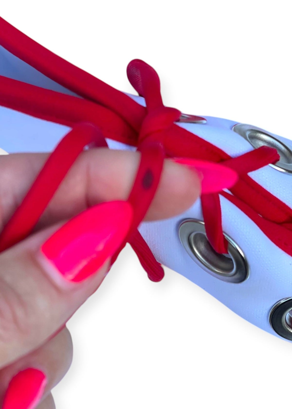 A close-up of a hand with bright pink fingernails tying red elastic cords through silver metal grommets on a white cylindrical strap.