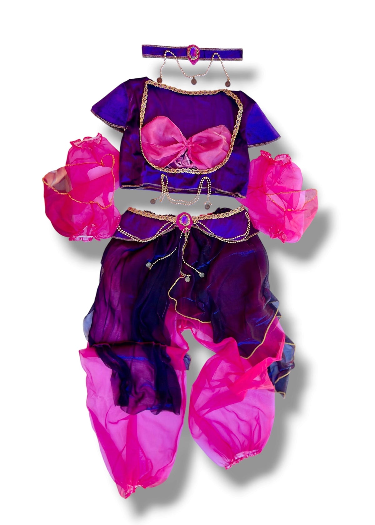 A children's belly dance costume set in purple and pink, featuring a short-sleeve crop top with a pink bow, matching purple pants with pink leg wraps, and pink flower arm accessories, displayed on a white background.
