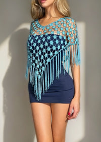 Woman wearing a blue and turquoise crochet poncho with fringe against a neutral background