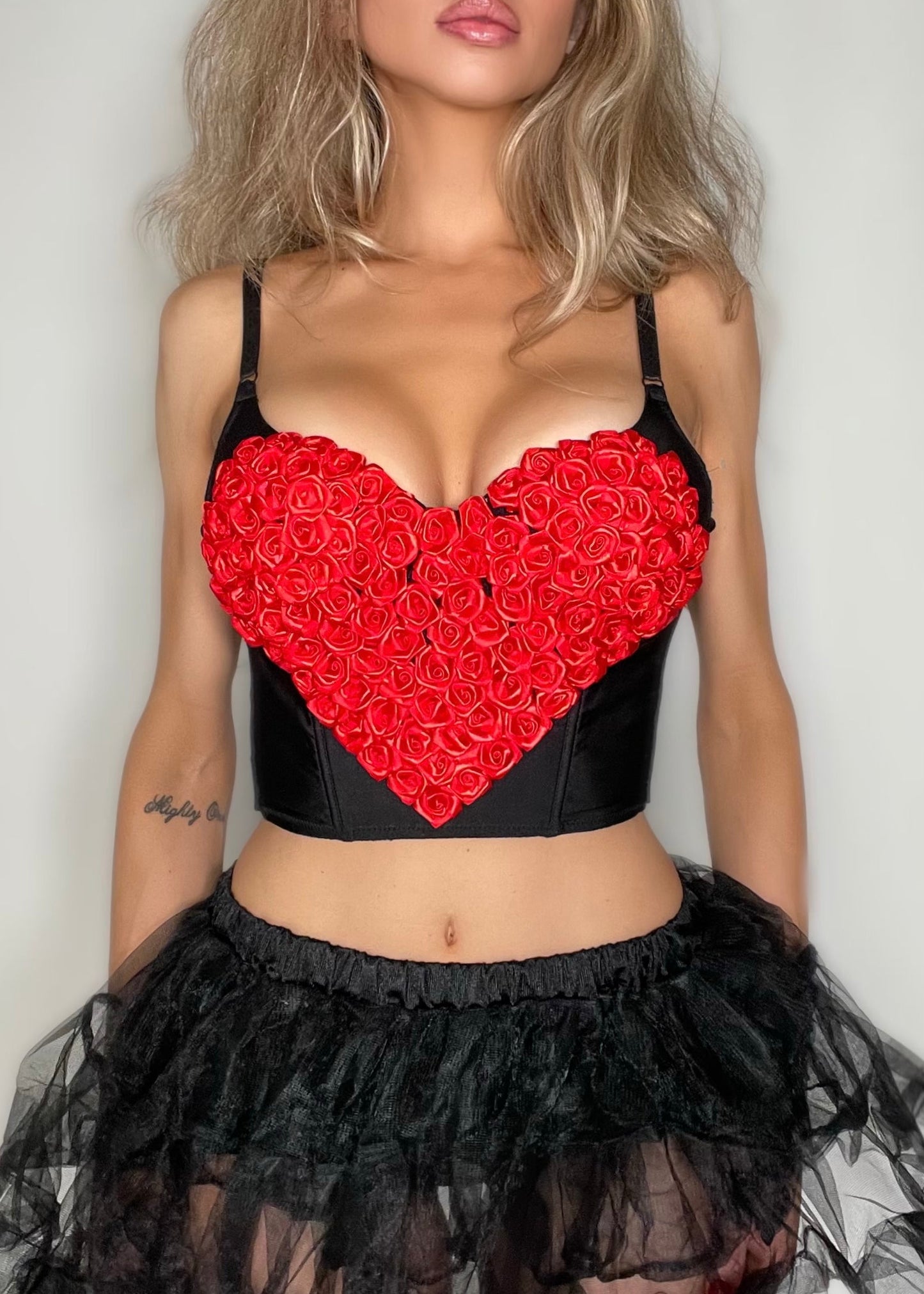 Person wearing a black top with a red heart design and a black tutu skirt on a plain background